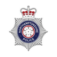 Northamptonshire Police badge featuring a silver starburst design with a central white rose on a blue circle. The badge is topped with a crown and the words Northamptonshire Police encircle the rose.